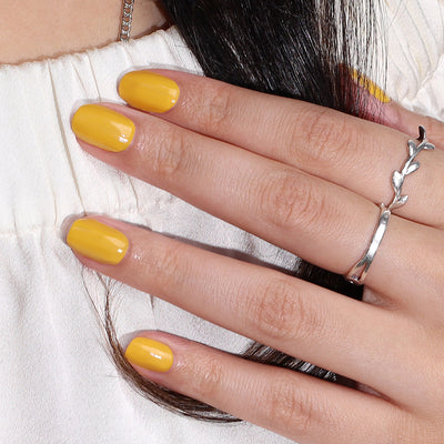 A hand with cheerful Daisy Chain canary yellow-painted nails, adorned with a LONDONTOWN silver ring featuring a twig design, rests on a white fabric.