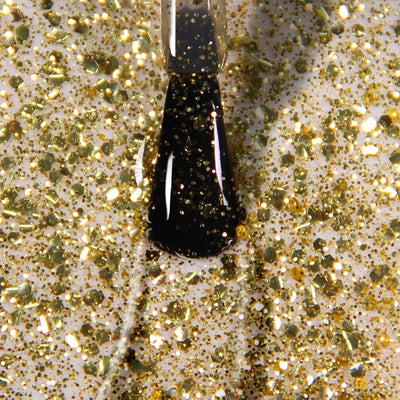 A nail polish brush applying LONDONTOWN Britannia gold glitter nail polish with a transparent base on a surface.