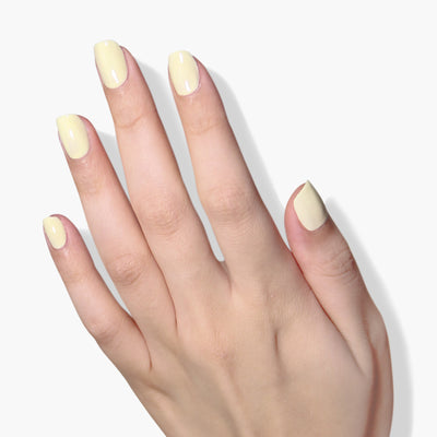 A hand with neatly manicured nails painted in Buttercup, a pastel yellow creme 16+ free, vegan, and cruelty-free nail polish by LONDONTOWN.