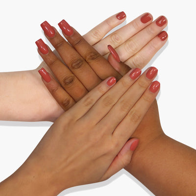 Four hands with varying skin tones, each adorned with red-painted nails, intersect and rest on top of each other against a white background, showcasing the vibrant Cactus Coral (Professional) vegan nail polish by LONDONTOWN.