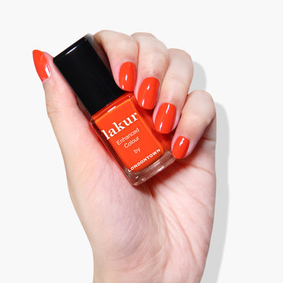 A hand with manicured nails holds a bottle of LONDONTOWN's Camden Chic nail polish in a bright red shade, showcasing its vegan and cruelty-free formula.