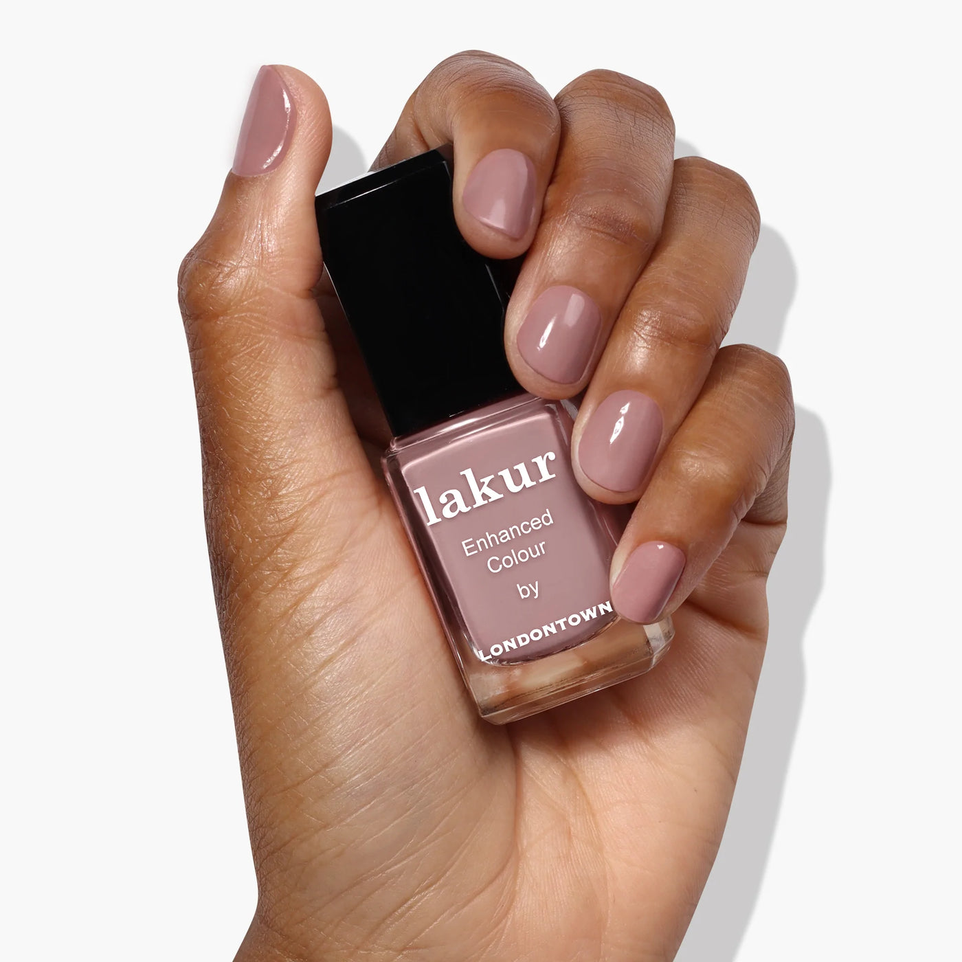 A hand holding a bottle of LONDONTOWN Chai (Professional) nail polish, the nails perfectly coated in a rich crème spiced taupe shade that matches the bottle seamlessly.