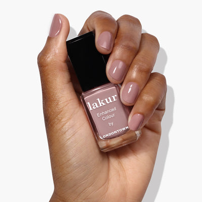 A hand holding a bottle of LONDONTOWN Chai (Professional) nail polish, the nails perfectly coated in a rich crème spiced taupe shade that matches the bottle seamlessly.