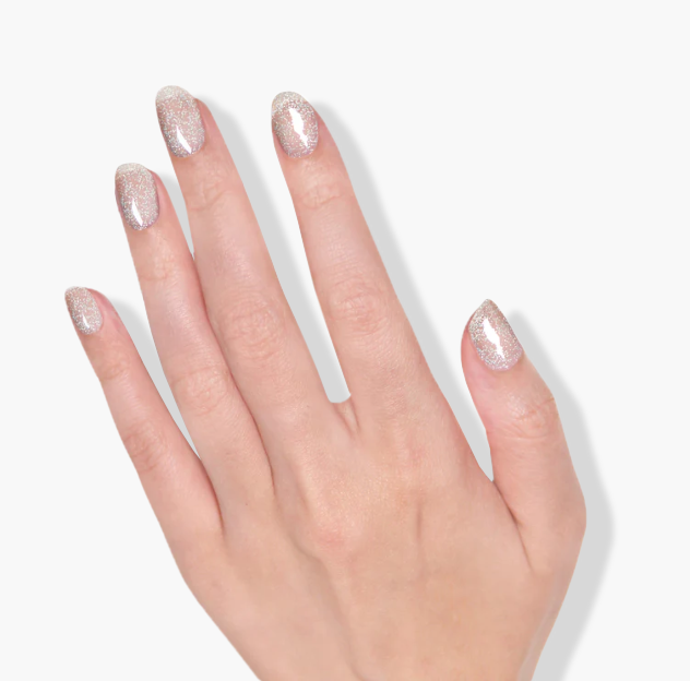 A hand with pale skin shows glittery, oval-shaped nails against a white background, enhanced by Cheshire Plains, a blue glitter cruelty-free nail polish from LONDONTOWN.