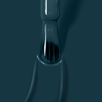 Close-up of a nail polish brush coated with LONDONTOWN's dark-colored, vegan nail polish "Chivvy Along," with the bristles partially visible against a dark green background.