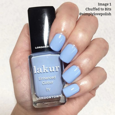 A hand with light blue polished nails is holding a bottle of "Chuffed to Bits (Professional)" nail polish by LONDONTOWN, a vegan and cruelty-free nail polish.