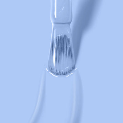 Close-up of a paintbrush with Chuffed to Bits (Professional) by LONDONTOWN paint in light blue, periwinkle crème blue. The bristles are saturated with the paint, and a drip is forming at the tip. The background is uniformly light blue.