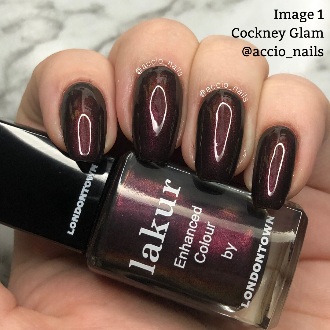 A hand with long nails painted dark red with a glossy finish holds a matching bottle of "Cockney Glam by LONDONTOWN," featuring a red-toned metallic crème. This PETA-certified, vegan, cruelty-free polish ensures your manicure is both stunning and ethically sound.