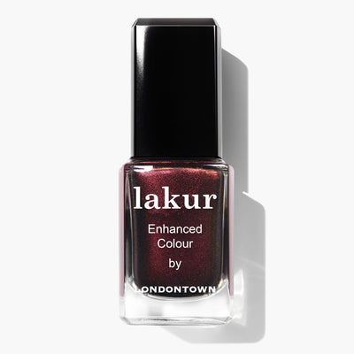 A bottle of LONDONTOWN's Cockney Glam Lakur enhanced color nail lacquer features a dark, shimmering, red-toned metallic crème. This PETA certified, vegan cruelty-free polish ensures an ethical and glamorous manicure.