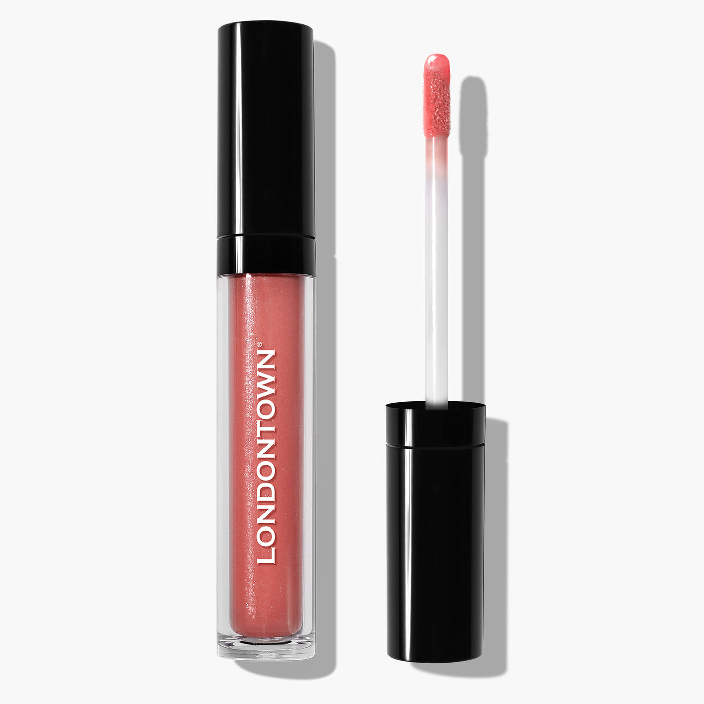 A tube of Plush Shine Lip Gloss in the shade Dainty, featuring a doe-foot applicator, labeled "LONDONTOWN" on the side, is shown with the applicator placed next to it. The coral pink hue gives a perfect sun-kissed glow.
