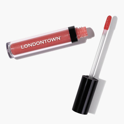 A tube of LONDONTOWN's Plush Shine Lip Gloss - Dainty with the wand applicator resting beside it on a white background. The kissed-by-the-sun shade is a stunning pinkish-red color.