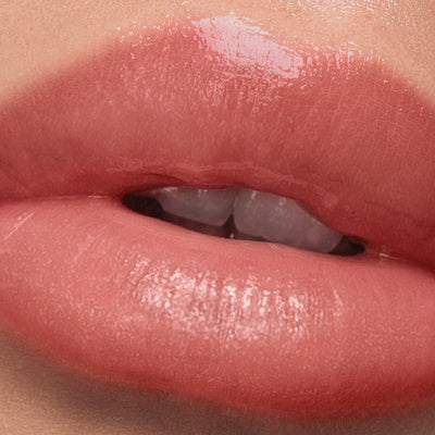 Close-up image of well-lit, glossy coral lips slightly parted, showcasing the details of the lip texture and sun-kissed shine from LONDONTOWN's Plush Shine Lip Gloss in Dainty.