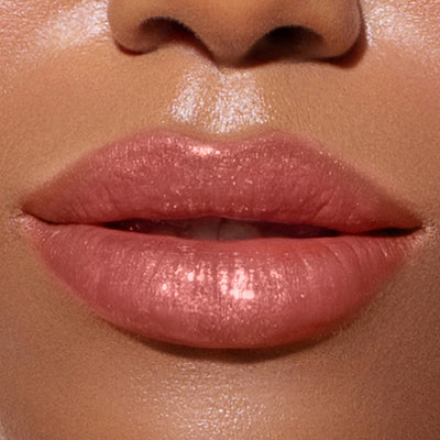 Close-up image of a person's glossy, coral-pink lips slightly parted, showcasing LONDONTOWN's Plush Shine Lip Gloss in "Dainty," creating a shimmering, sun-kissed effect.
