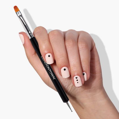A hand with a beige manicure featuring black minimalist designs, including delicate dots on each nail, holds the Dot & Detail Nail Art Tool by LONDONTOWN.