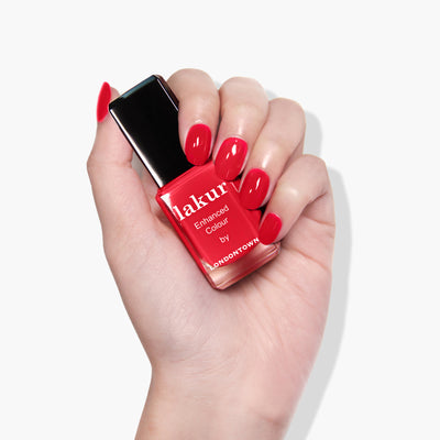 A hand holding a bottle of red nail polish labeled "Down to Dilly" by LONDONTOWN, against a white background. LONDONTOWN polishes are known for being vegan and cruelty-free, adding an ethical touch to your manicure collection.