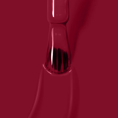 Close-up of a nail polish brush applying glossy Dragon Fruit, a vegan and cruelty-free nail polish by LONDONTOWN, on a surface.