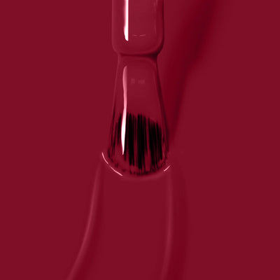 Close-up of LONDONTOWN's Dragon Fruit (Professional) vegan, cruelty-free nail polish brush coated with red polish, hovering just above a smooth, glossy surface of red nail polish.
