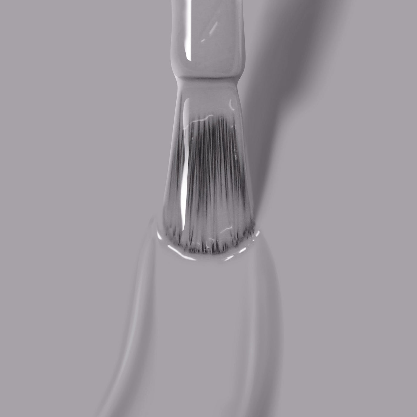 Close-up of a LONDONTOWN paintbrush with white bristles dipped in Earl Grey nail polish on a gray background.