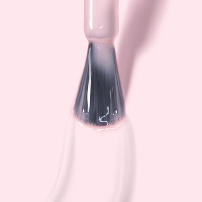 A close-up image of a nail polish brush with LONDONTOWN's Fairy Charming gel color in light pink against a pale pink background, showcasing its super pigmented formula.
