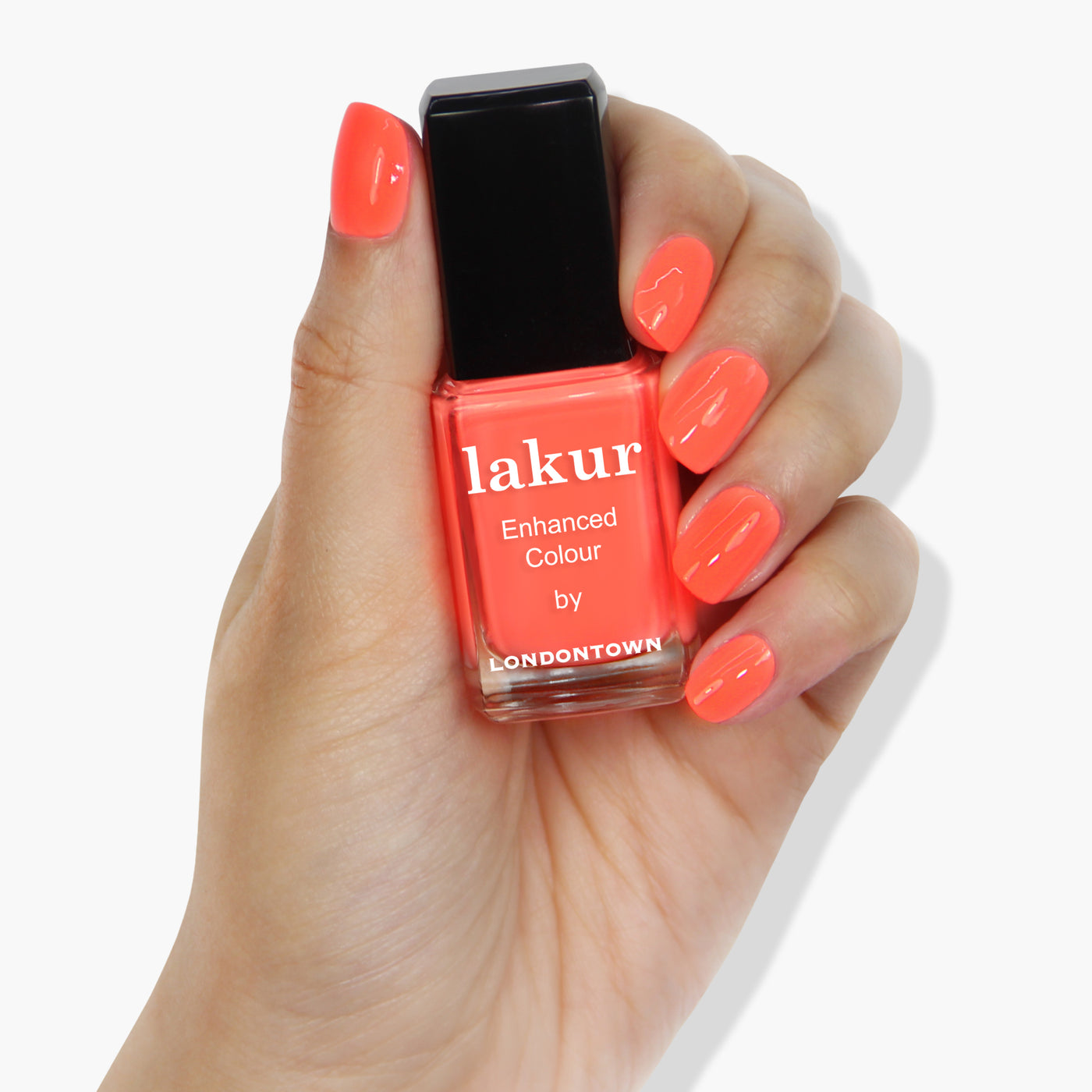 A hand with manicured nails holds a bottle of LONDONTOWN's Flashback nail polish in a radiant sunset orange shade, showcasing its vibrant hue.