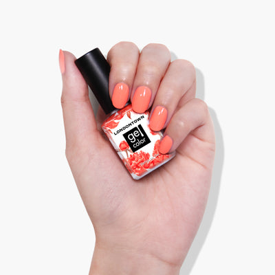 A hand with painted nails holds a bottle of LONDONTOWN's Flashback gel color nail polish in a vibrant neon orange shade, perfect for use with UV/LED light.