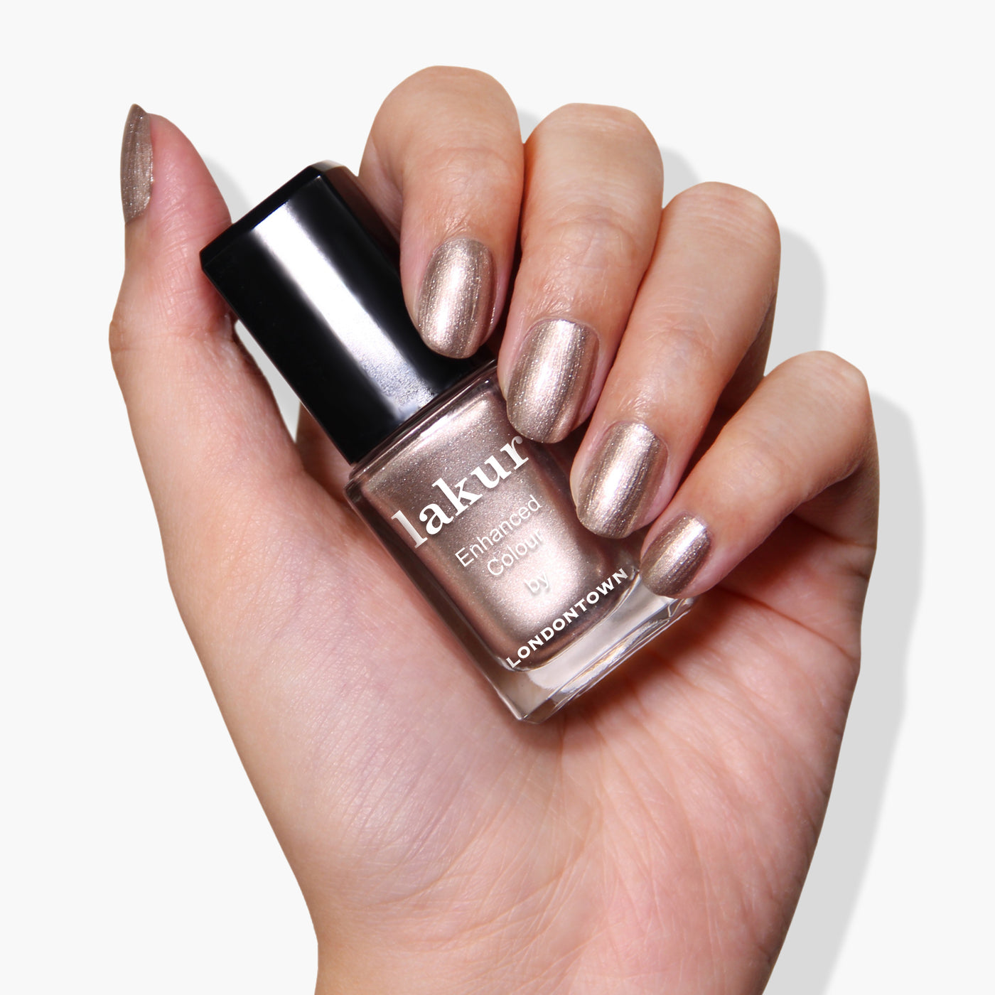 A hand with metallic, shimmery nails holds a bottle of LONDONTOWN's PETA certified, vegan cruelty-free Lakur nail polish in the shade Gilded.