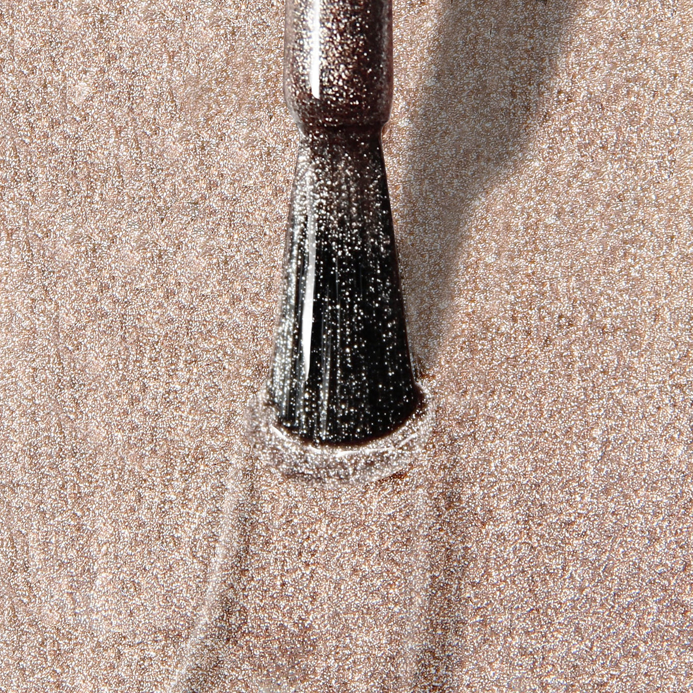 Close-up of a Gilded (Professional) makeup brush from LONDONTOWN applying shimmery powder on a textured surface. The bristles are coated with the sparkling substance, reminiscent of the elegant sheen you get from champagne nail polish.