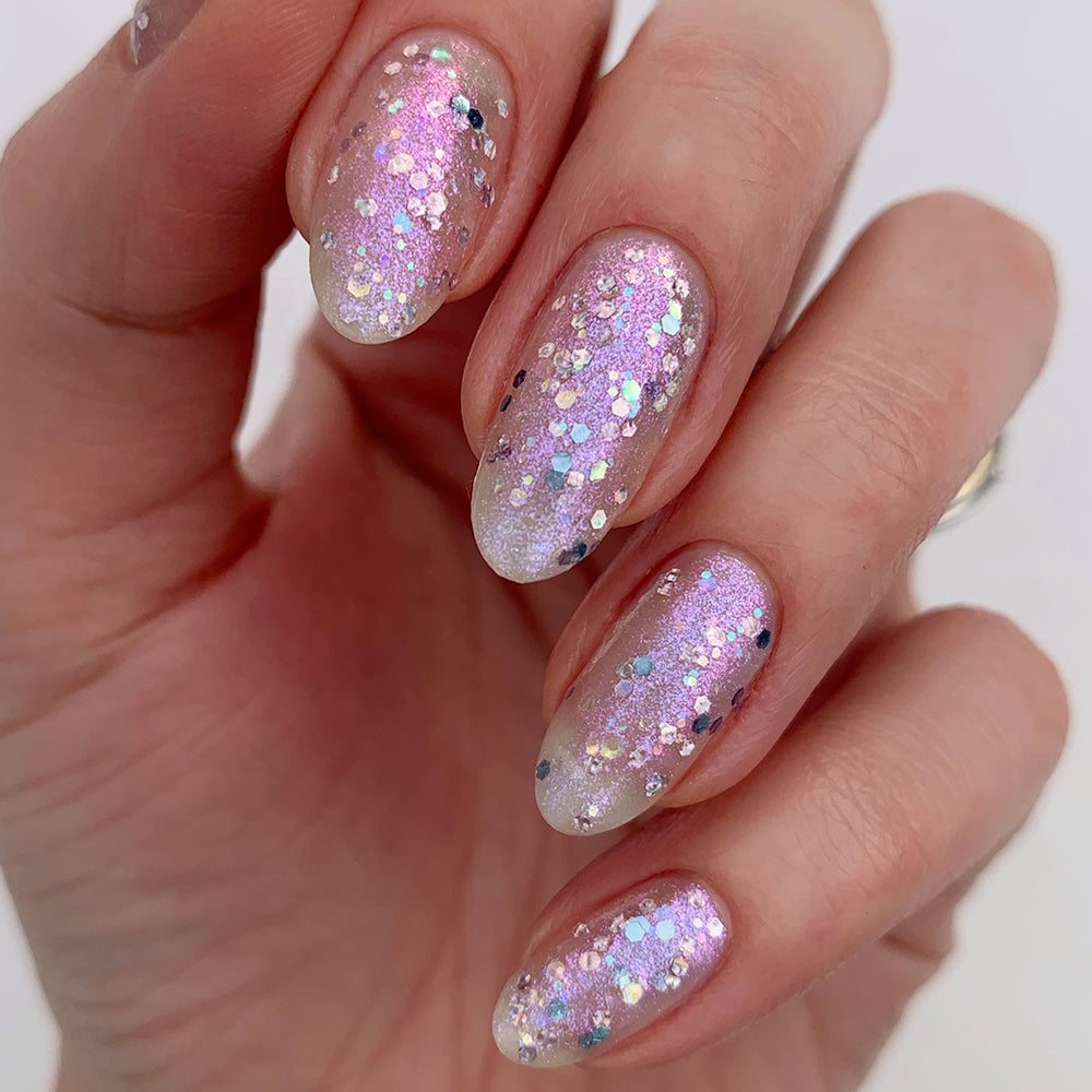 A hand with almond-shaped nails painted in LONDONTOWN's Grape Fizz, adorned with holographic purple glitter.