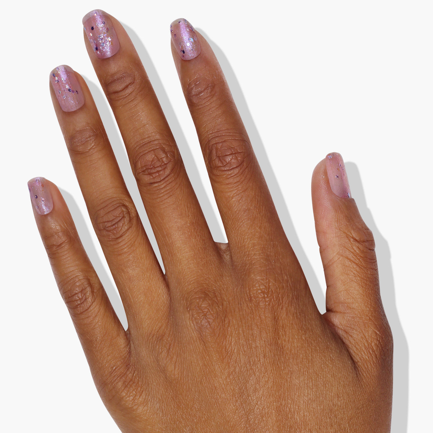 Close-up of a hand with polished fingernails painted in LONDONTOWN's Grape Fizz. The nails shimmer beautifully against a plain white background, showcasing the captivating holographic purple glitter.