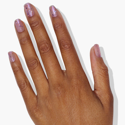 Close-up of a hand with polished fingernails painted in LONDONTOWN's Grape Fizz. The nails shimmer beautifully against a plain white background, showcasing the captivating holographic purple glitter.