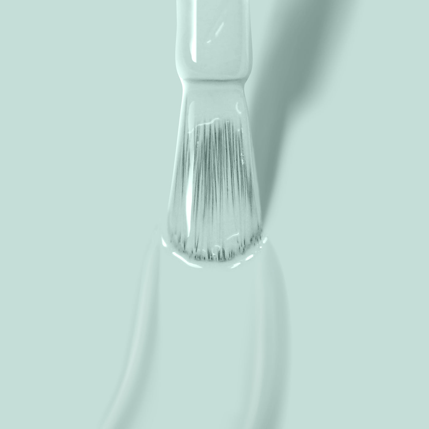 Close-up of a paintbrush with LONDONTOWN's Mint No Chip paint on its bristles, reminiscent of mint creme, against a light green background.