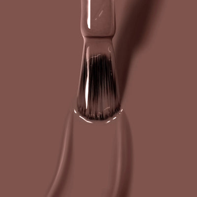 A close-up view of a paintbrush in use, with bristles coated in a thick layer of LONDONTOWN's Mudslide (Professional) deep brown nail polish.