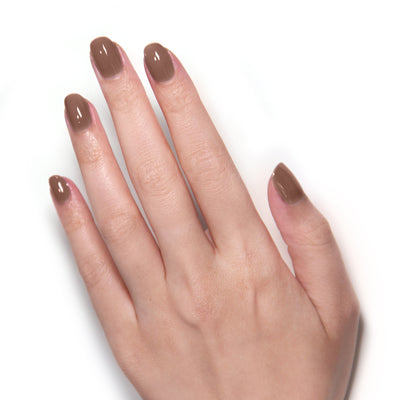 A close-up of a person's hand adorned with LONDONTOWN's Mudslide nail polish, featuring a stunning beige accent, set against a white background.