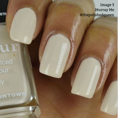 Close-up of a hand with light beige polished nails, holding a bottle of vegan, cruelty-free nail polish labeled "Murray Me'' by LONDONTOWN. The French vanilla cream hue adds an elegant touch.