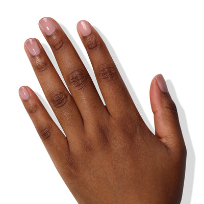 A hand with dark skin displaying five fingers. The nails, short and neatly trimmed, showcase a hint of color using LONDONTOWN's Perfecting Nail Veil #4 in a light pink shade. The white background casts faint shadows of the fingers, emphasizing every detail.
