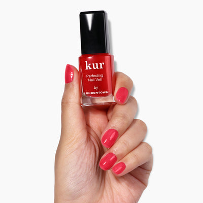 A hand with neatly painted nails in a vibrant red shade holds a bottle of LONDONTOWN's "Perfecting Nail Veil #8" nail polish, showcasing its care and powerful color.