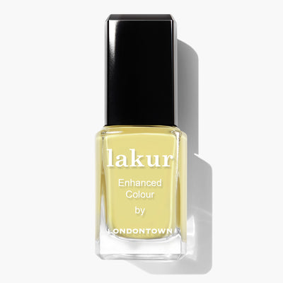 A bottle of LONDONTOWN's Lakur nail polish called "Notting the Fancy" in a light lemon meringue yellow shade with a black cap. The bottle features "Enhanced Colour by Londontown" and highlights its cruelty-free formula.