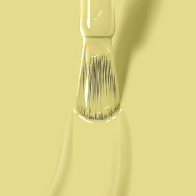 A close-up of a LONDONTOWN Notting the Fancy (Professional) paintbrush with beige bristles, coated in light yellow paint reminiscent of lemon meringue yellow nail polish, set against a matching yellow background.