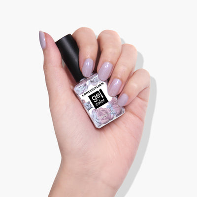 Hand holding a LONDONTOWN Opal Gel Color nail polish bottle with shimmering lilac-colored fingernails, perfect for your next UV/LED light manicure session.