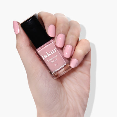 A hand holds a bottle of pastel pink nail polish labeled "Out of Office (Professional) by LONDONTOWN," with nails painted in a matching shade. This vegan, cruelty-free, and 16+ free formula ensures a guilt-free, vibrant look.