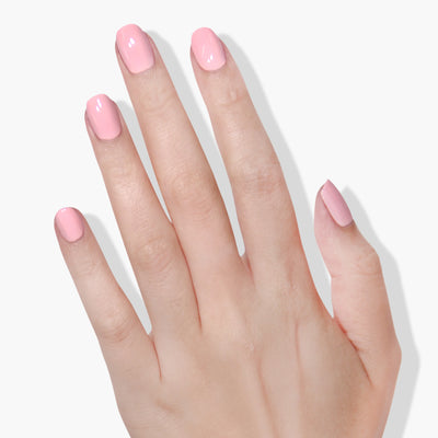 A hand with manicured nails painted in LONDONTOWN's Out of Office (Professional) pastel pink nail polish against a plain white background, showcasing its 16+ Free and vegan cruelty-free formula.