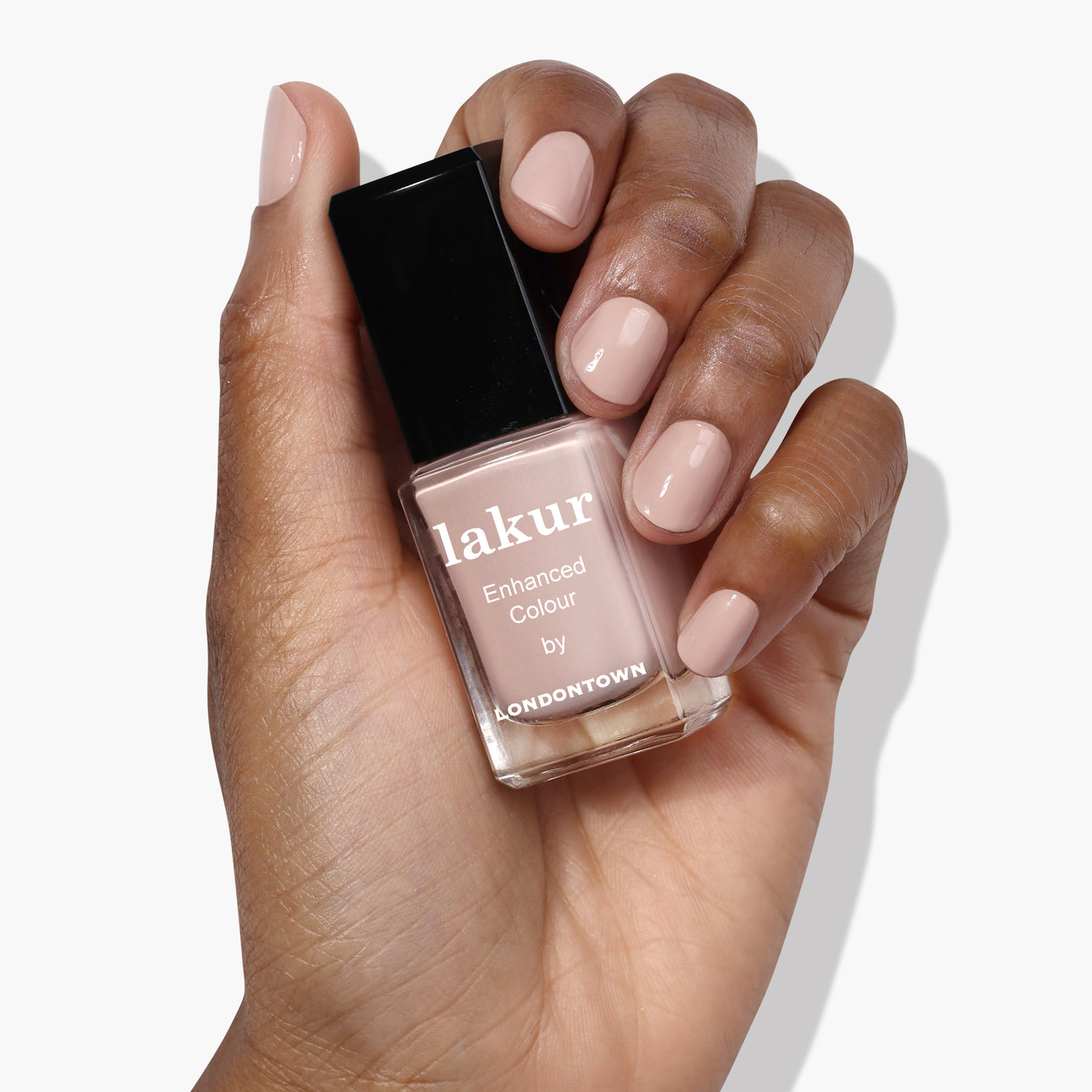 A hand holding a bottle of Pampas Beige by LONDONTOWN nail polish in a creamy beige shade. The nails are painted in the same buff color as the polish.