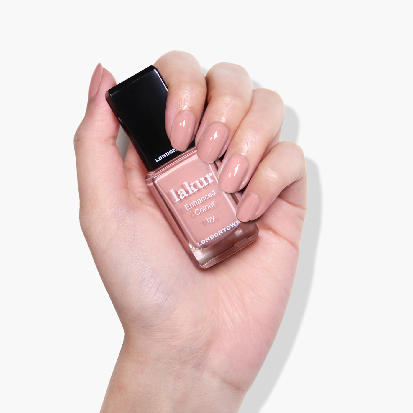 A hand holding a bottle of LONDONTOWN Peach Please nail polish in a pale peach creme shade with well-manicured nails painted in the same vegan, cruelty-free color.