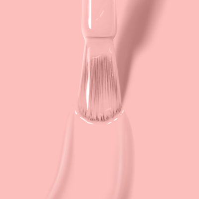 Close-up of a brush being dipped in LONDONTOWN's vegan cruelty-free Peach Please nail polish against a pink background.