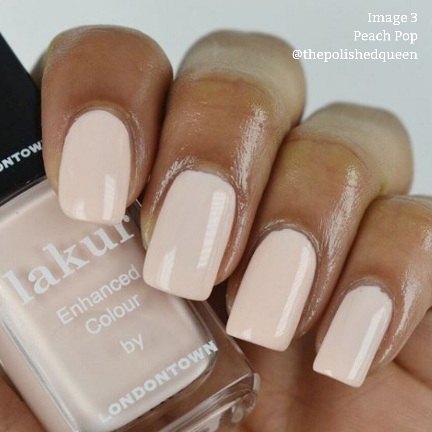 Close-up of a hand with manicured nails painted in a glossy peach shade. A cruelty-free, vegan nail polish bottle labeled "Peach Pop by LONDONTOWN" is held between the fingers.