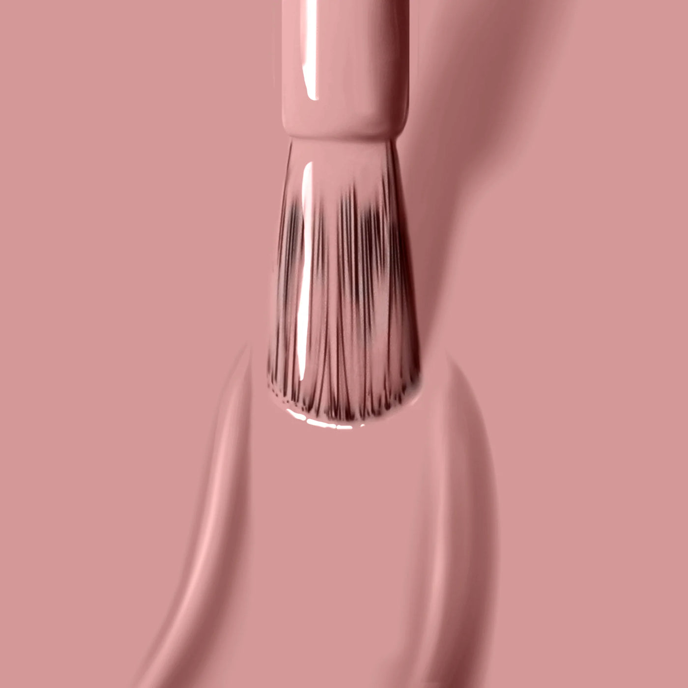 Close-up of a LONDONTOWN brush applying Pink Sands (Professional), light pink, vegan cruelty-free nail polish with visible bristles and smooth strokes on a matching pink background.