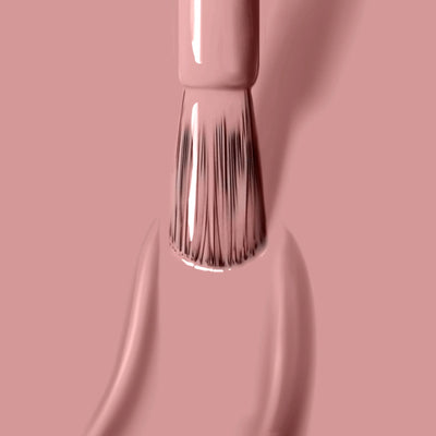 Close-up of a LONDONTOWN brush applying Pink Sands (Professional), light pink, vegan cruelty-free nail polish with visible bristles and smooth strokes on a matching pink background.