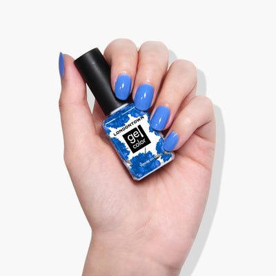 A hand with blue-painted nails holds a bottle of LONDONTOWN Poolside Dreams against a white background, ready for a perfect finish under UV/LED light.