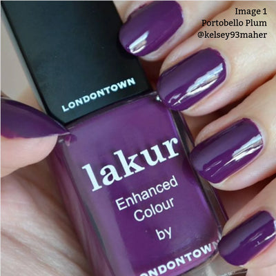 Close-up of hands with freshly manicured nails painted in a deep warm plum crème, holding a bottle of LONDONTOWN nail polish labeled "lakur - Enhanced Colour." Text on the image reads "Portobello Plum (Professional)," highlighting this vegan, cruelty-free nail polish.