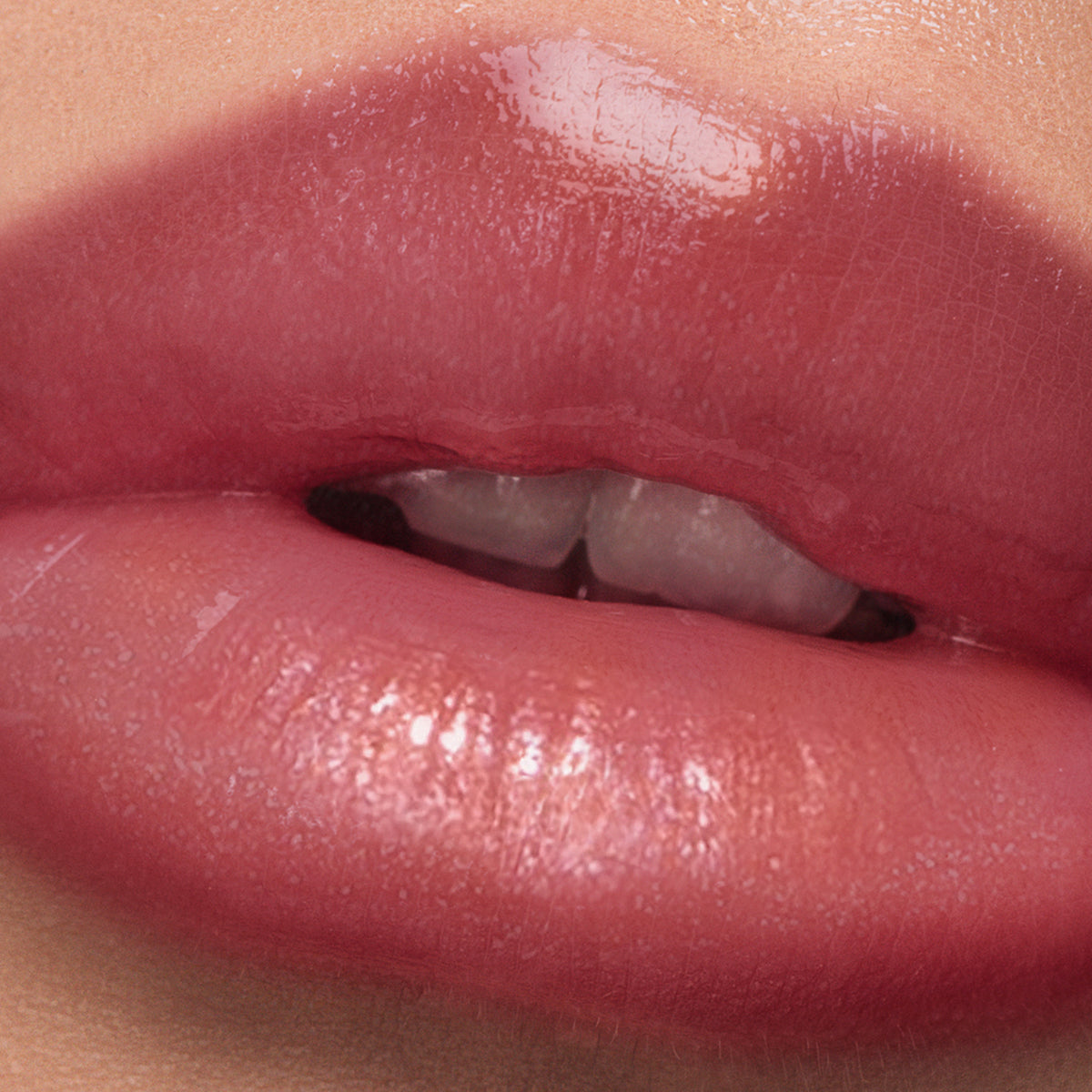 A close-up of glossy, flushed pink-tinted lips enhanced by LONDONTOWN's Plush Shine Lip Gloss in Posh, with slightly parted teeth visible.